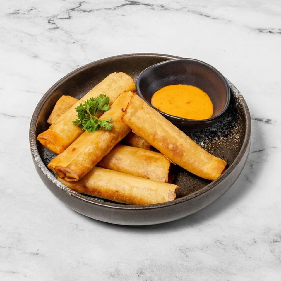 Crispy golden spring rolls garnished with parsley, served in a dark bowl with orange dipping sauce on a marble surface.